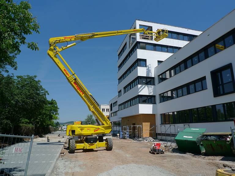 Eine Gelenkteleskoparbeitsbühne im Einsatz auf einer Baustelle, auf welcher ein moderner Neubau eines Unternehmens entsteht.